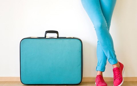 A person standing next a blue suitcase