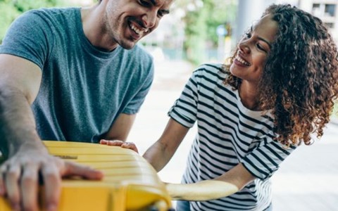 A smiling couple packing a suitcase into a car