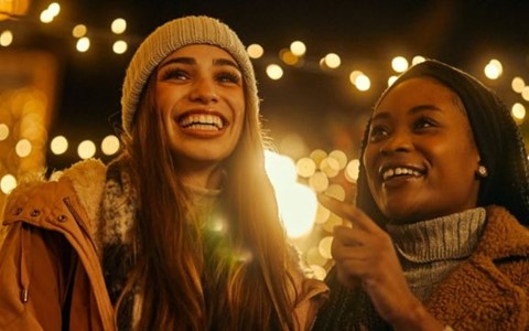 two smiling women standing in front of Christmas lights