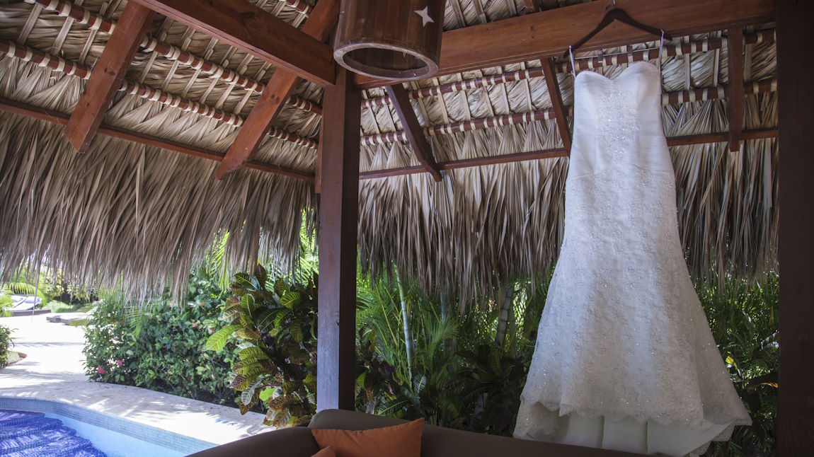 A wedding dress hangs from the beams of a covered patio in a tropical villa.