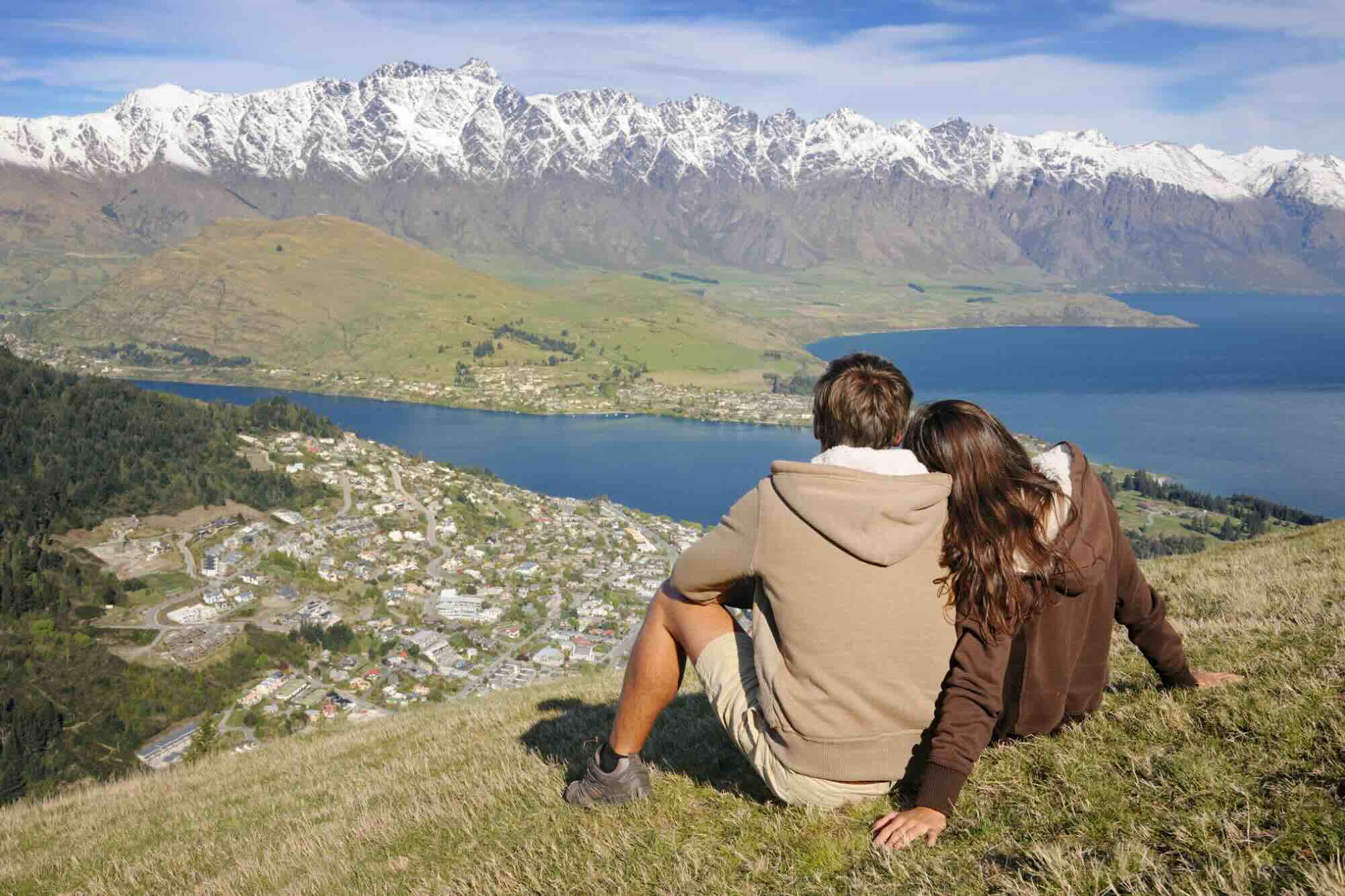 A couple sits on a hillside overlooking Queenstown, New Zealand. 